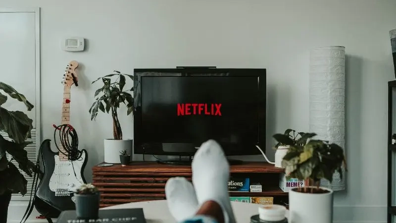 Hand holding Roku remote pointing at television that is blurred out in the background.